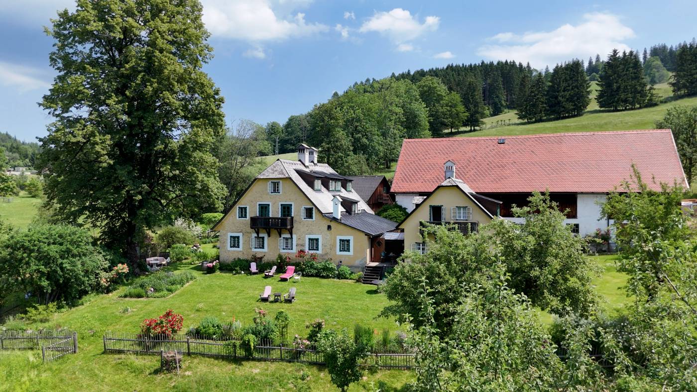 Hof Berneck's stone farmhouse facade surrounded by gardens in the Austrian mountains