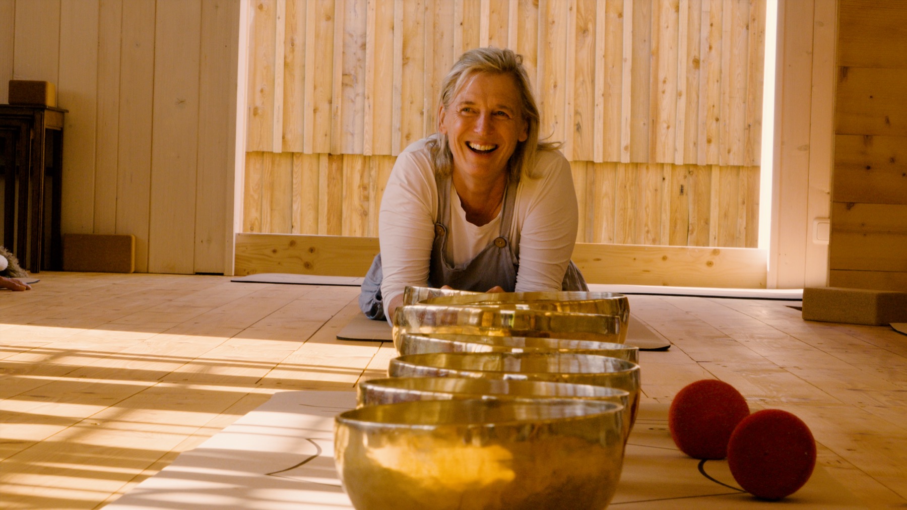 Mariella laughing beside a row of singing bowls in the sunlit yoga studio at Hof Berneck