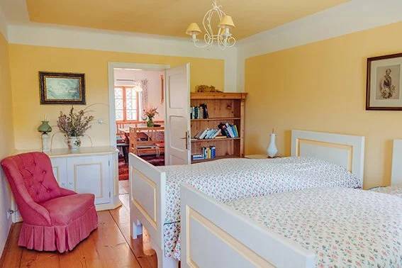 Blush pink armchair beside a pine bookcase in the Twin Room With Bathroom